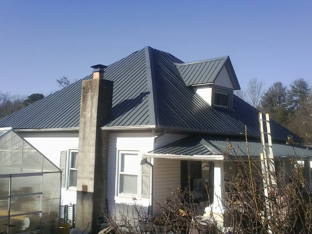 Dark blue standing seam metal roof on a white farmhouse with dormer — Slate & Tile Roof Repair by Roofing Brothers in Marble Rock