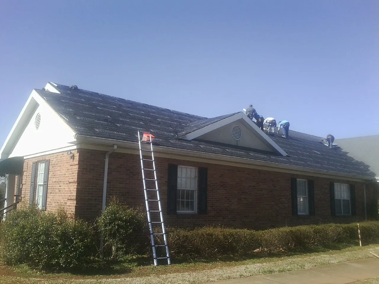 Crew tearing shingles off a brick ranch roof with a ladder set — Emergency Roof Repair work by our crew in Marble Rock