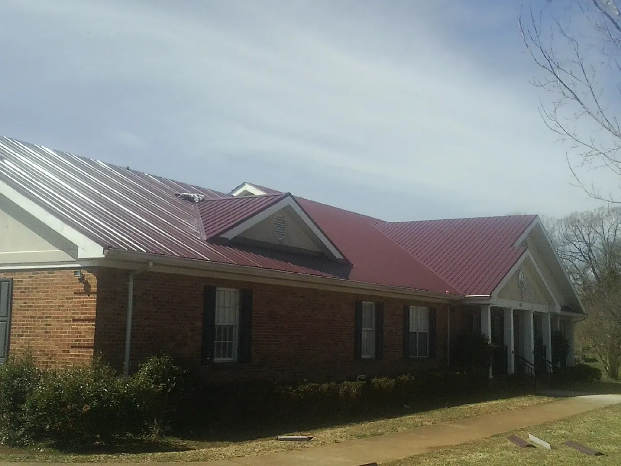 Red metal roof with gabled entries on a long brick building, from a Hail Damage Roof Repair job in Marble Rock