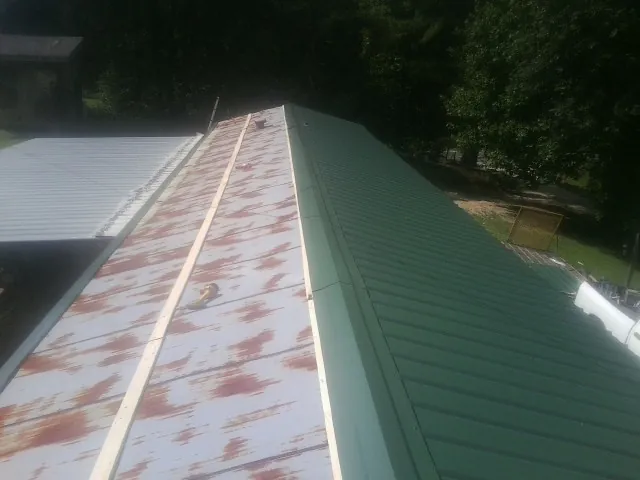 Old rusted panels beside newly installed green metal roofing in Marble Rock