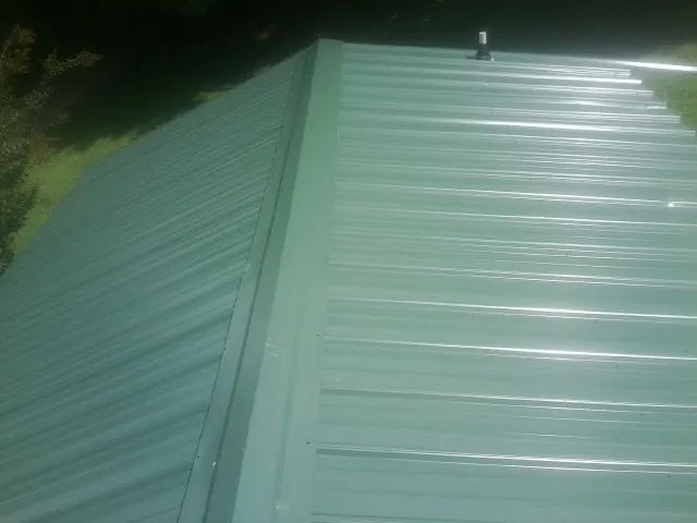 New green metal panels meeting at the ridge of a roof — Flat Roof Repair work by our crew in Marble Rock