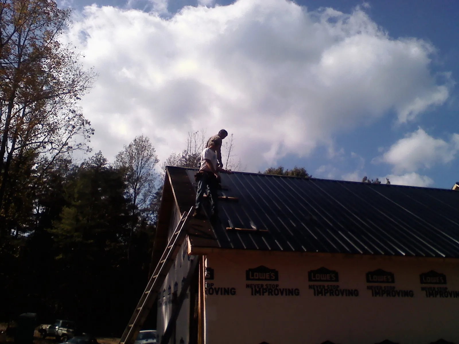 Roofer fastening dark metal panels high against a cloudy sky, from a Roof Inspection job in Marble Rock