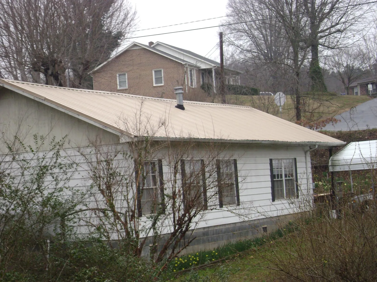 Tan metal roof on a white sided house set into a hillside — Commercial Roofing by Roofing Brothers in Marble Rock