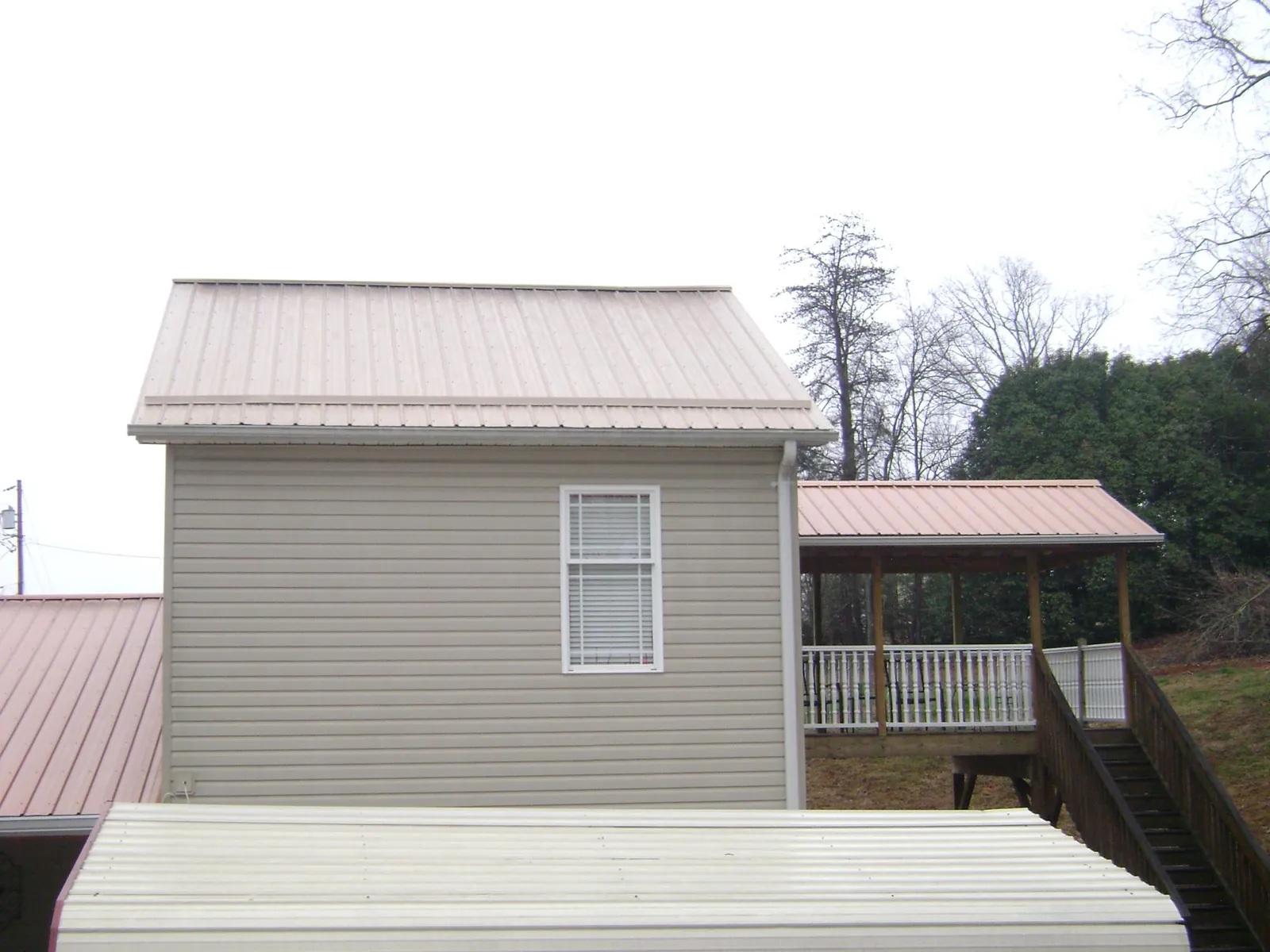 Tan metal roofs on a two story addition and attached porch, from a Roof Replacement job in Marble Rock